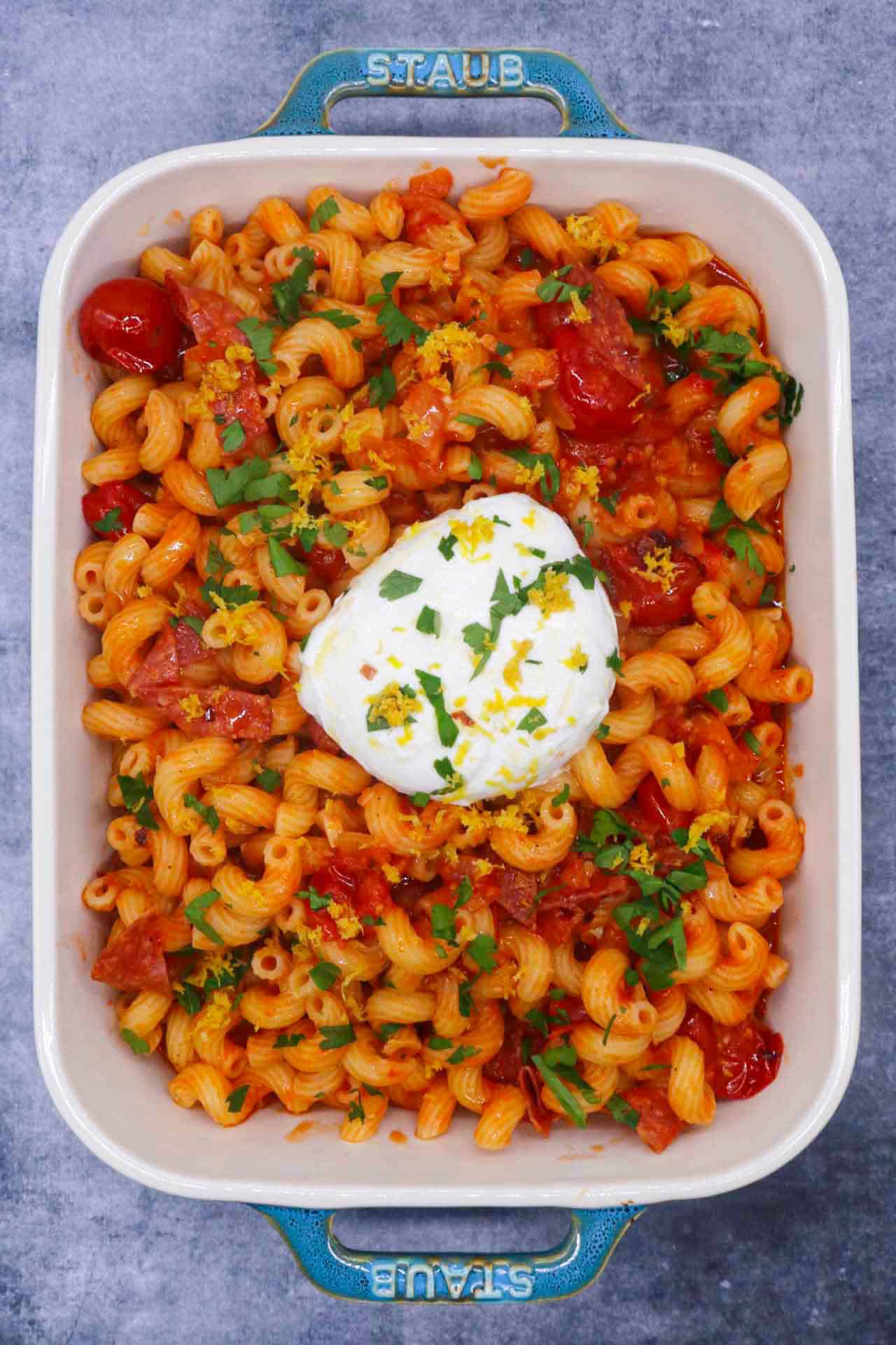 Tomato salami pasta with large ball of burrata in rectangle serving dish