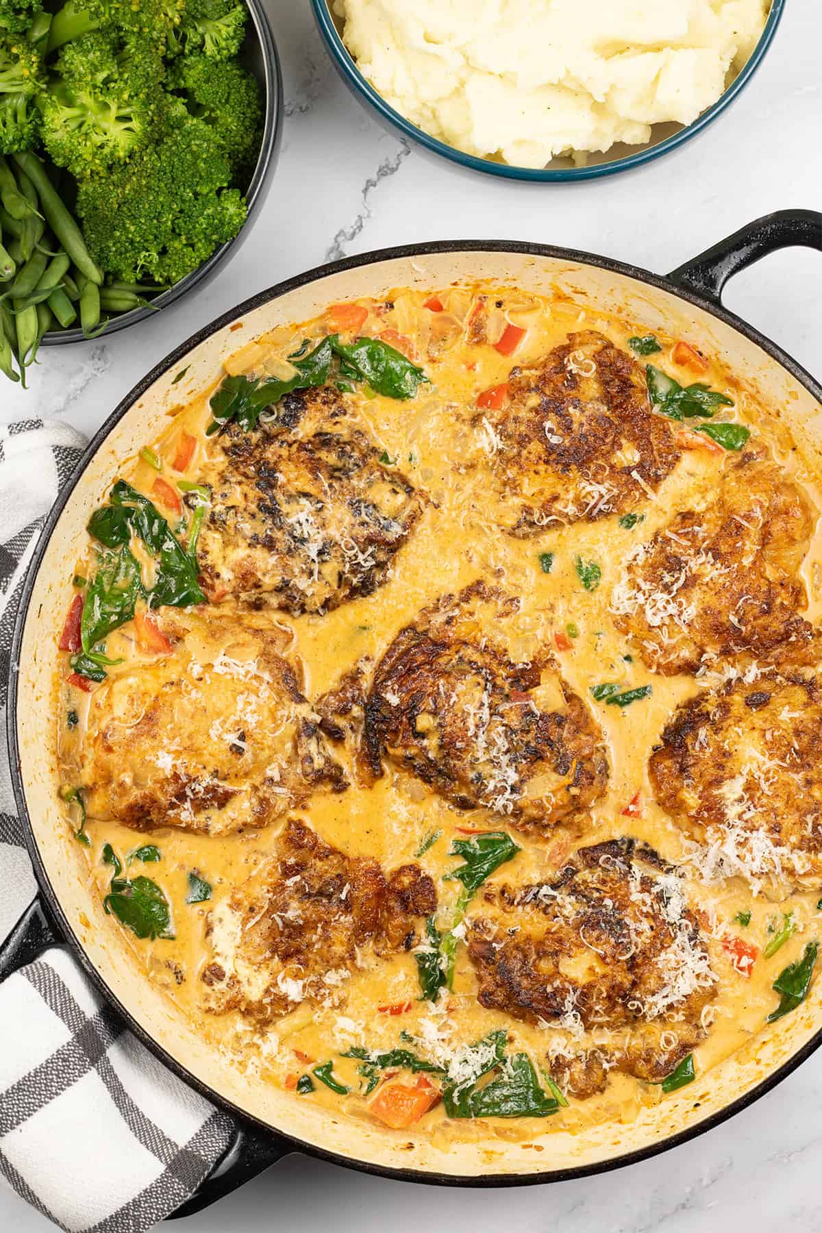 Tuscan chicken in large round casserole dish with bowls of green beans and broccoli, and mashed potatoes on the side.