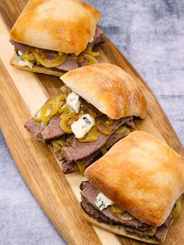 Three Brisket sandwiches with beer onions and blue cheese on a board