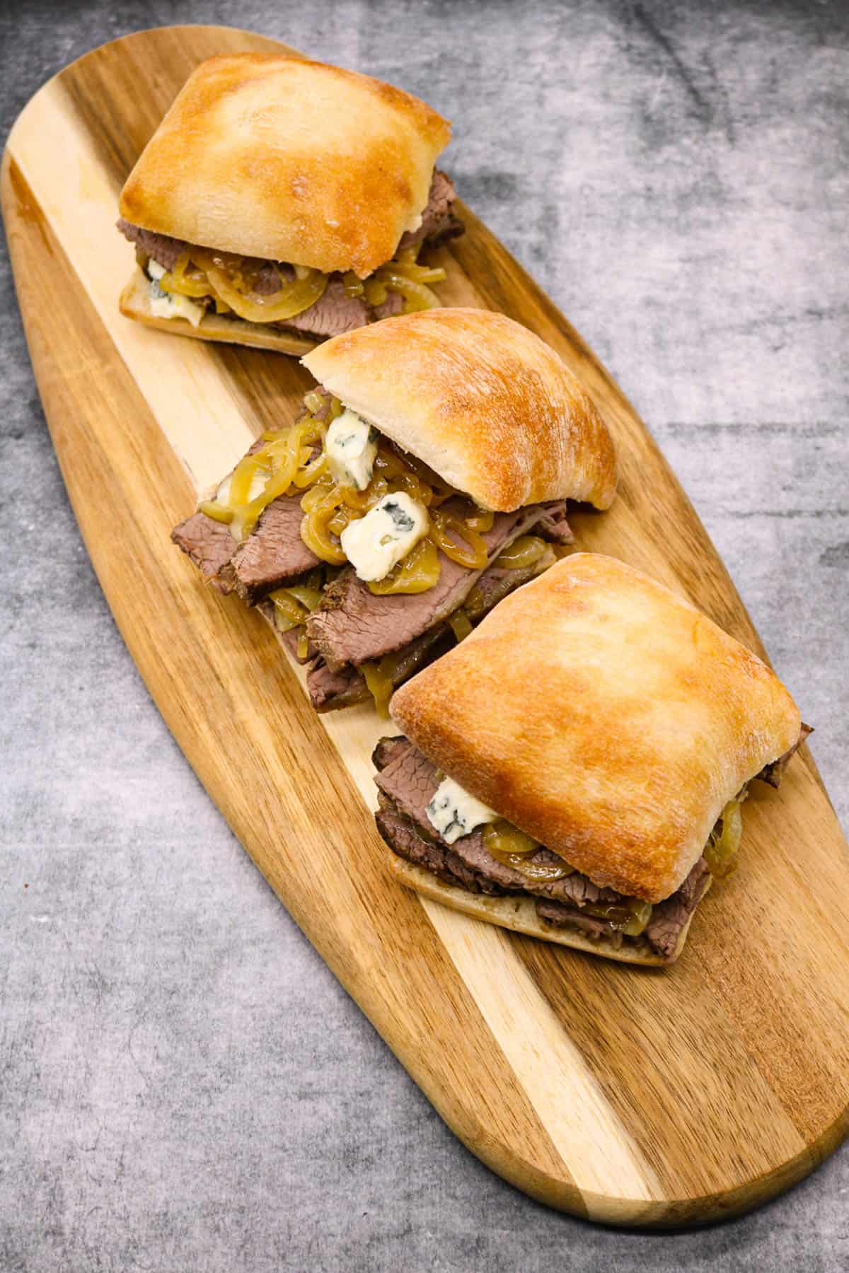 Three Brisket sandwiches with beer onions and blue cheese on a board