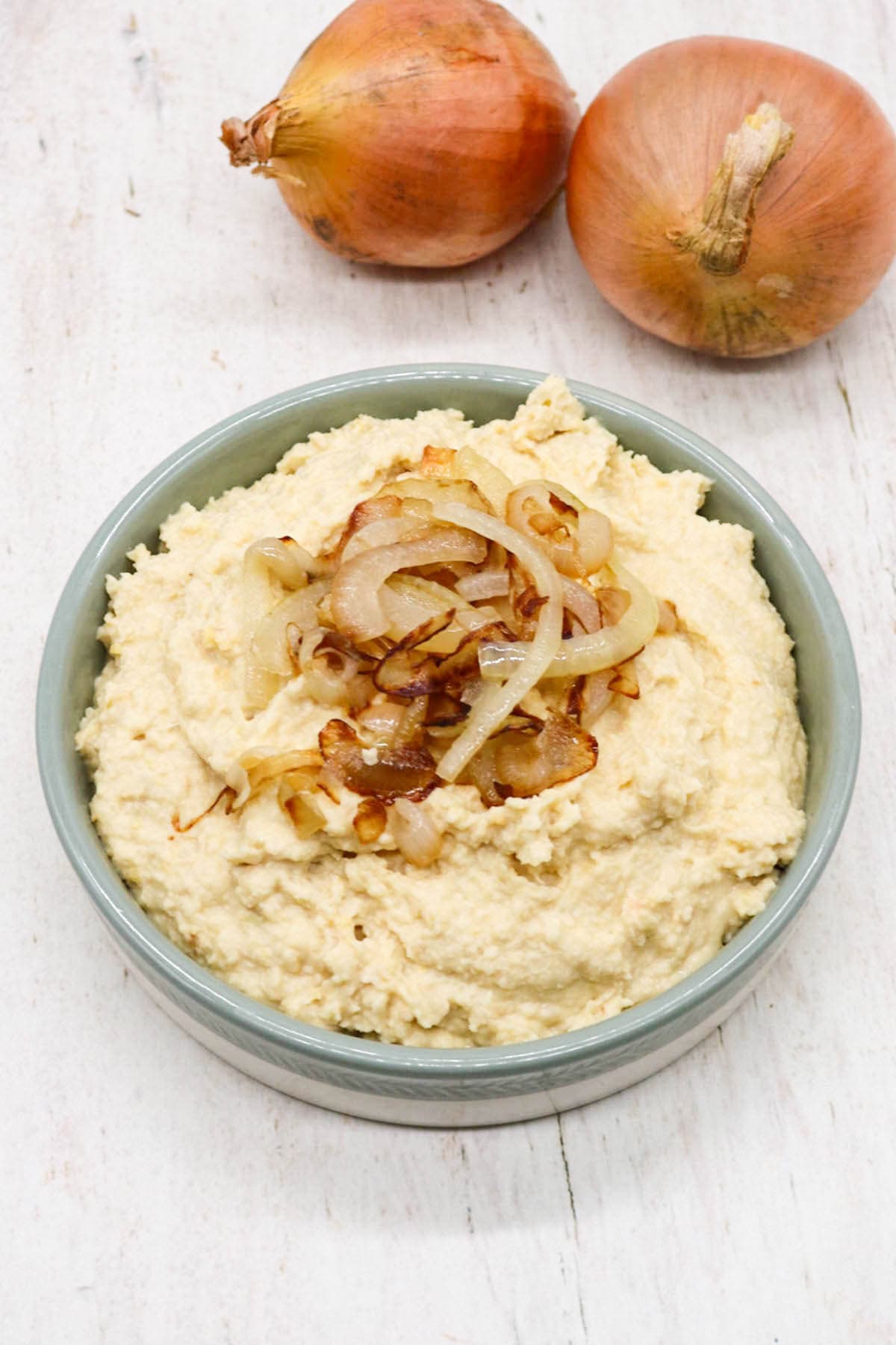 Caramelised onion houmous in bowl with onions on top and raw onions in background