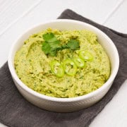 Coriander and green chilli humous in bowl with coriander and sliced chillis on top