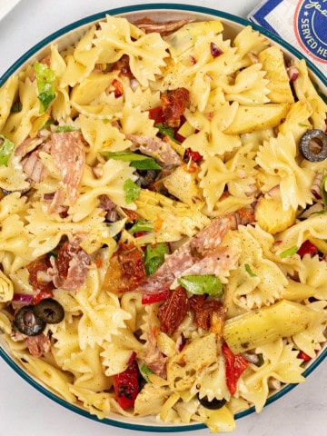 Deli pasta salad in a serving bowl with paper napkins on the side.