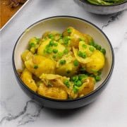 Easy crushed potatoes with peas in a black and cream serving bowl.