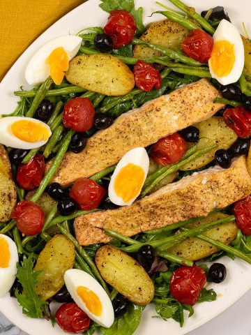 Easy salmon nicoise traybake on a white serving platter with a mustard napkin on the side.