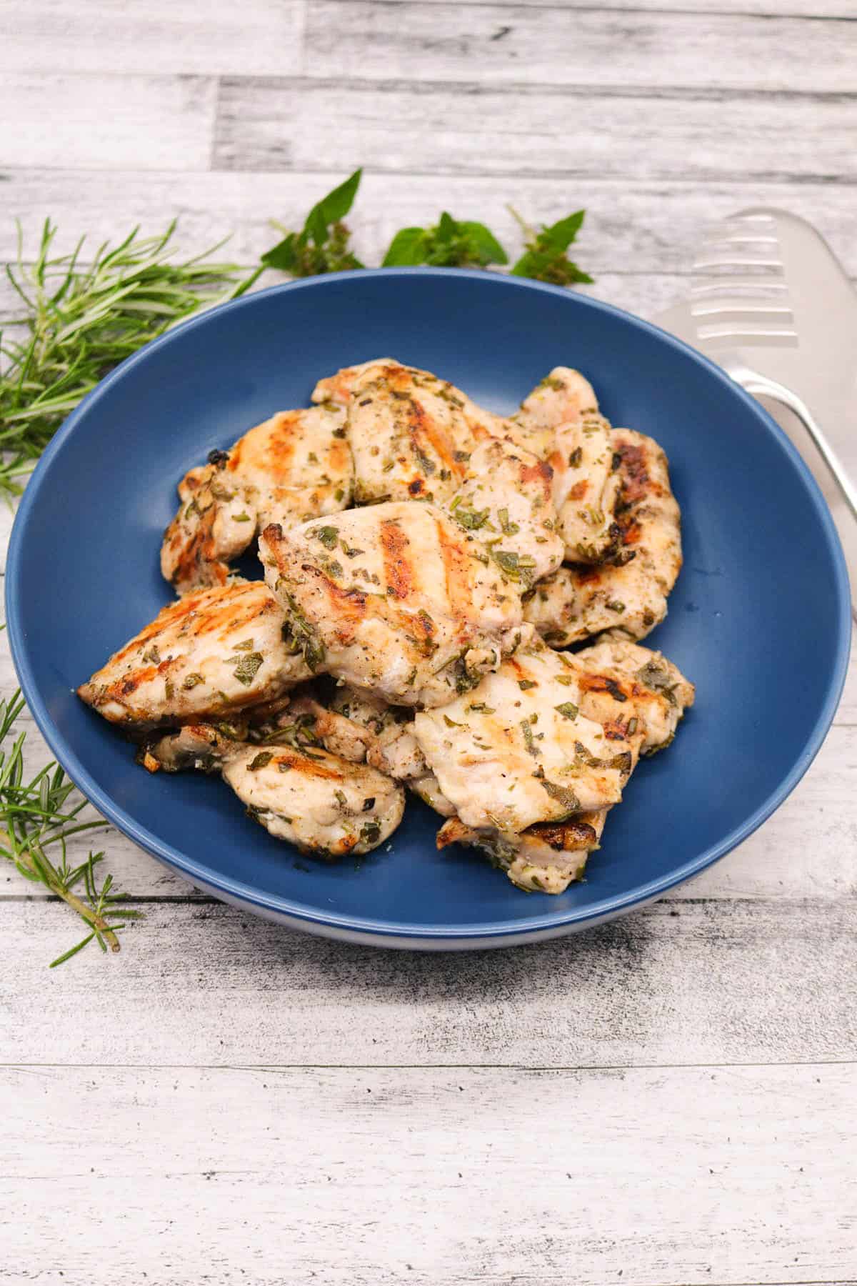 Lemon herb chicken thighs in blue bowl with mint and rosemary to the side