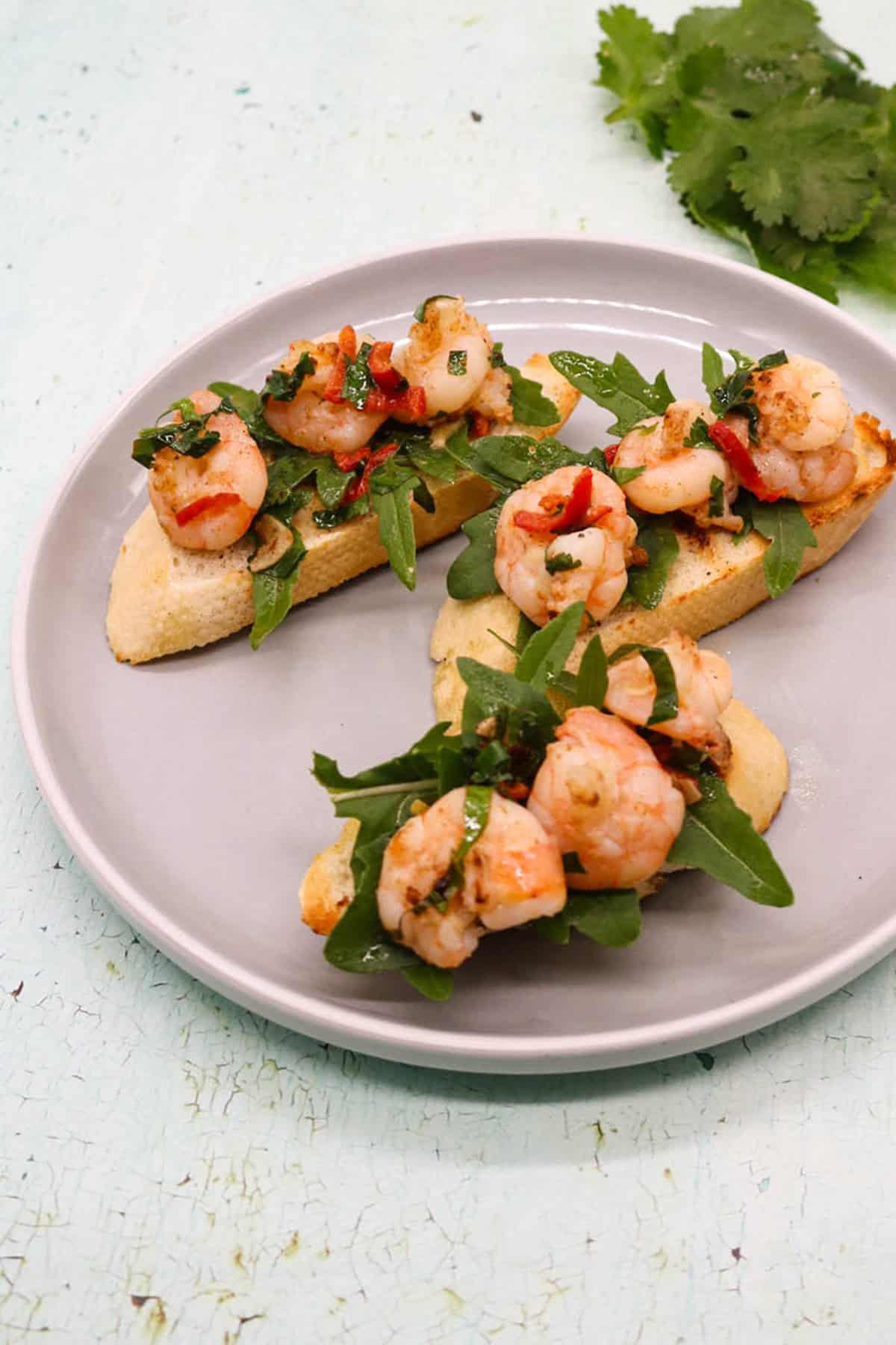 3 slices of lemony prawn bruschetta on a light grey side plate.