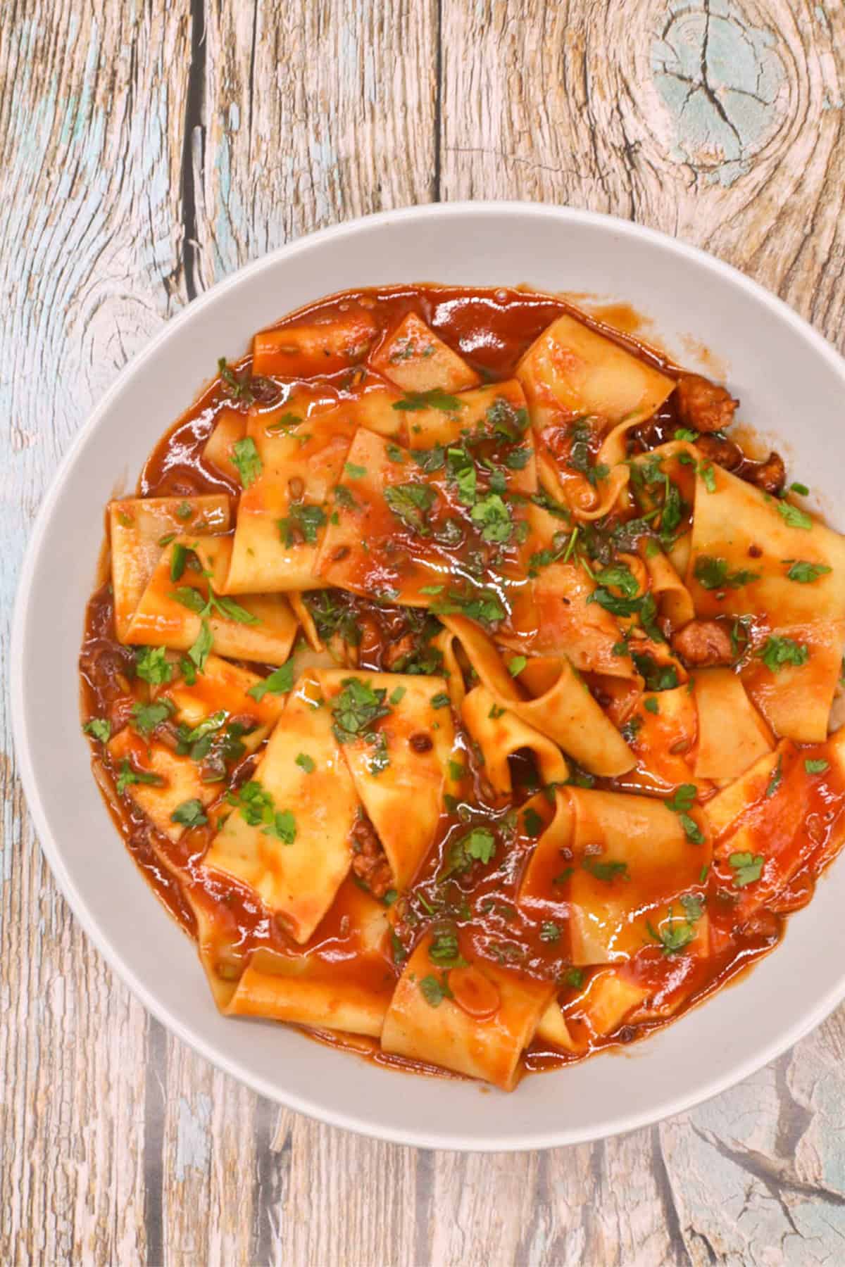 Sausage and pappardelle pasta in a light grey pasta bowl.