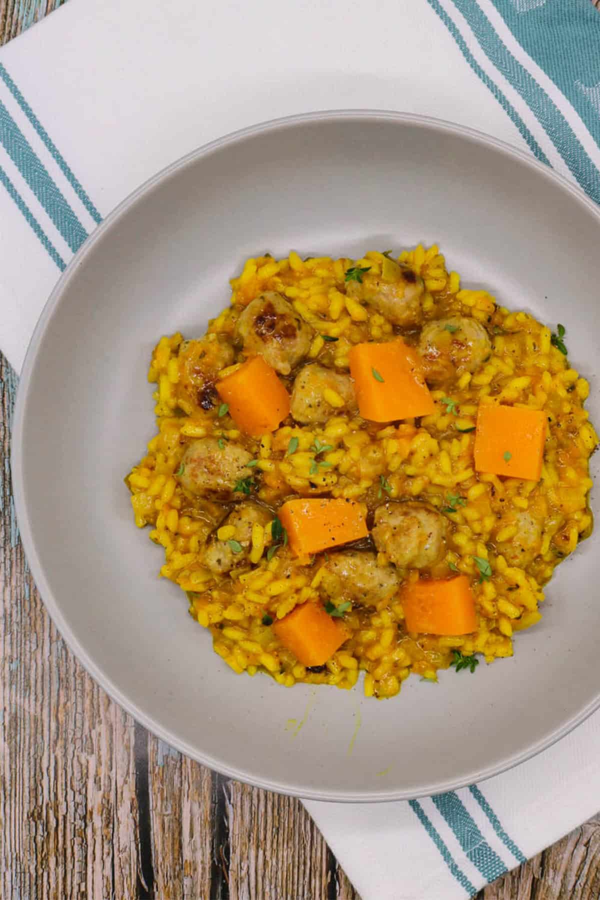 A portion of sausage and squash risotto in a grey bowl sitting on top of a teal green and white towel.
