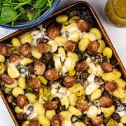 Sausage and taleggio gnocchi bake on a large baking tray with a bowl of baby salad leaves and a small jug of Italian dressing on the side.