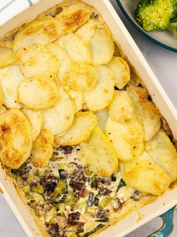 Smoked haddock, black pudding and leek gratin in a rectangle Staub dish with a bowl of broccoli and green beans on the side.