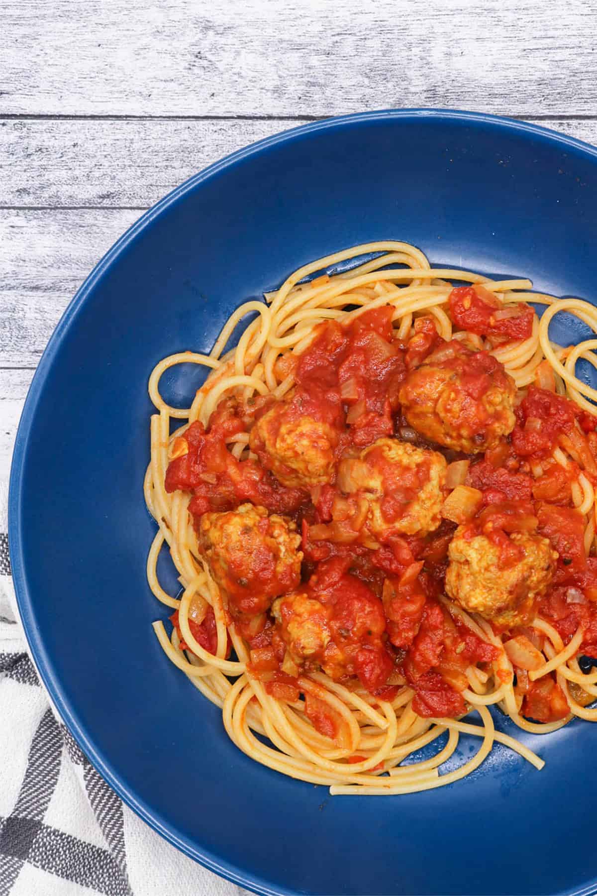 A portion of spicy sausage and meatball pasta in a dark blue bowl.