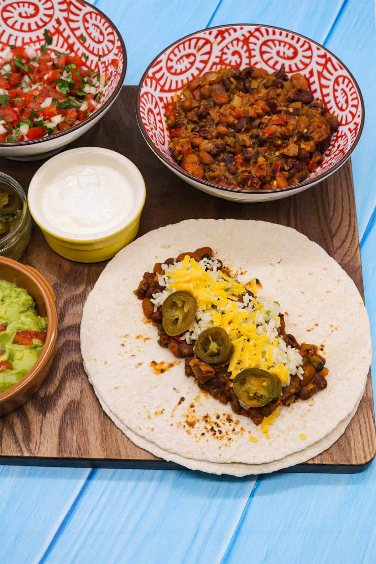 Veggie chilli on flour tortilla with rice jalapeños and cheese on wooden board