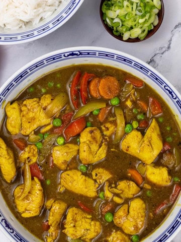 Fakeaway Chinese chicken curry in a blue and white oriental serving bowl with a bowl of rice and dish of sliced spring onions on the side.