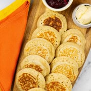 Homemade crumpets on a board with dishes of jam and butter.