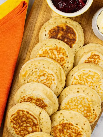 Homemade crumpets on a board with dishes of jam and butter.