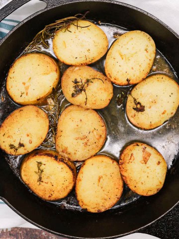 Buttery herbed melting potatoes in a skillet pan, sitting on a white and teal striped towel.