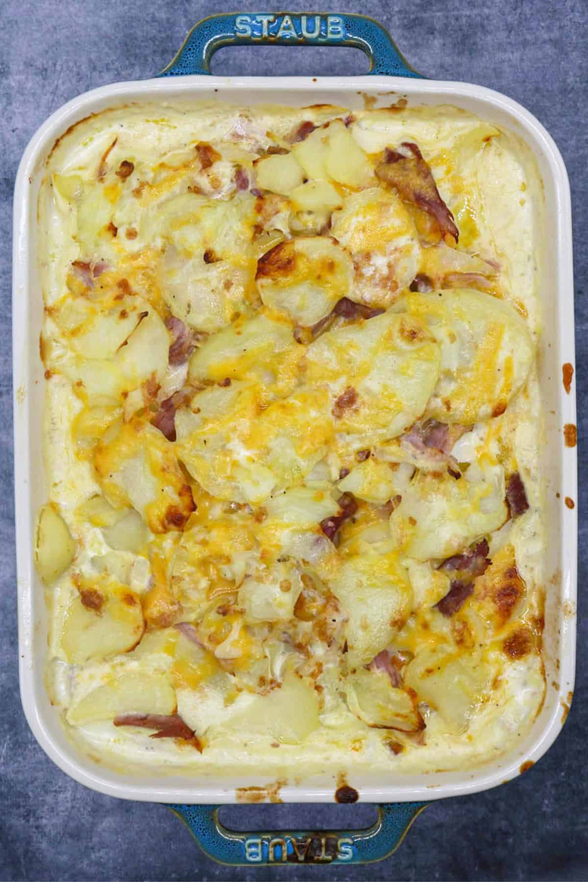 Cheesy potato and gammon bake in rectangular Staub oven dish.