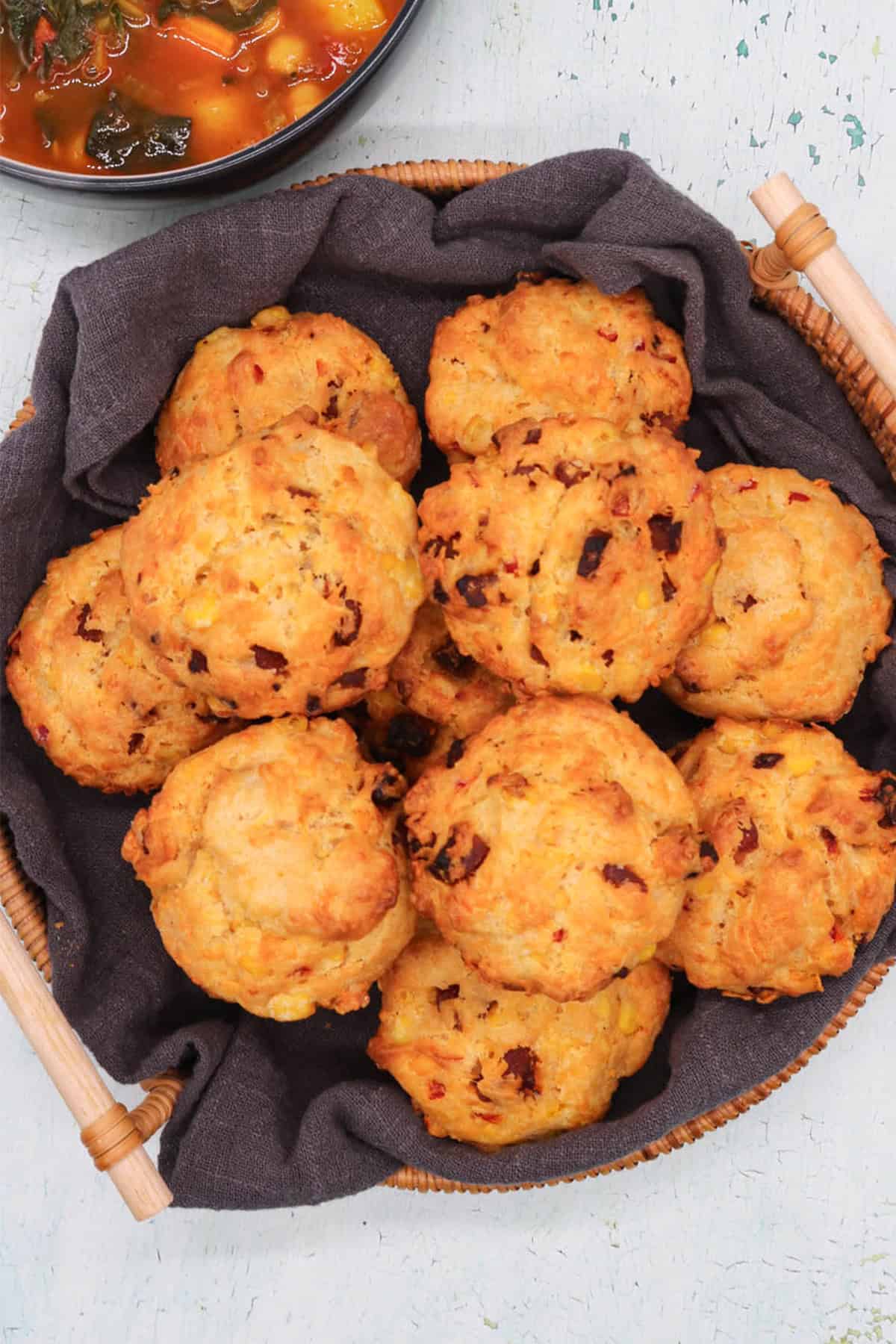 Chorizo, sweetcorn and chilli muffins in a bread basket, with a bowl of soup in the background.