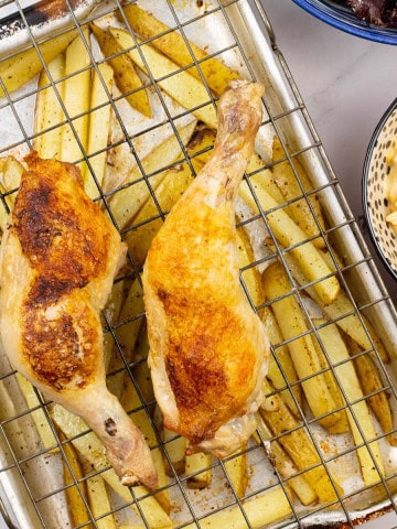 Easy chicken legs and chips traybake in a roasting tin with bowls of coleslaw and salad on the side.