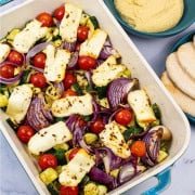 Halloumi and mediterranean veg tray bake in a large rectangle Staub dish, with pitta breads and houmous on the side.
