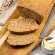 Classic wholemeal bread made in the Thermomix on a board with 2 slices cut and a small dish of butter with butter knife on the side.