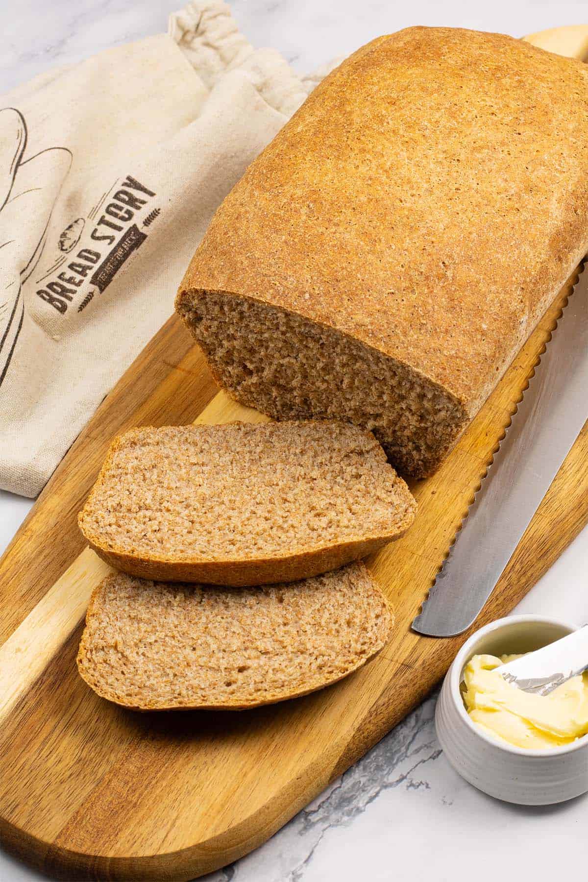 Classic wholemeal bread made in the Thermomix on a board with 2 slices cut and a small dish of butter with butter knife on the side.