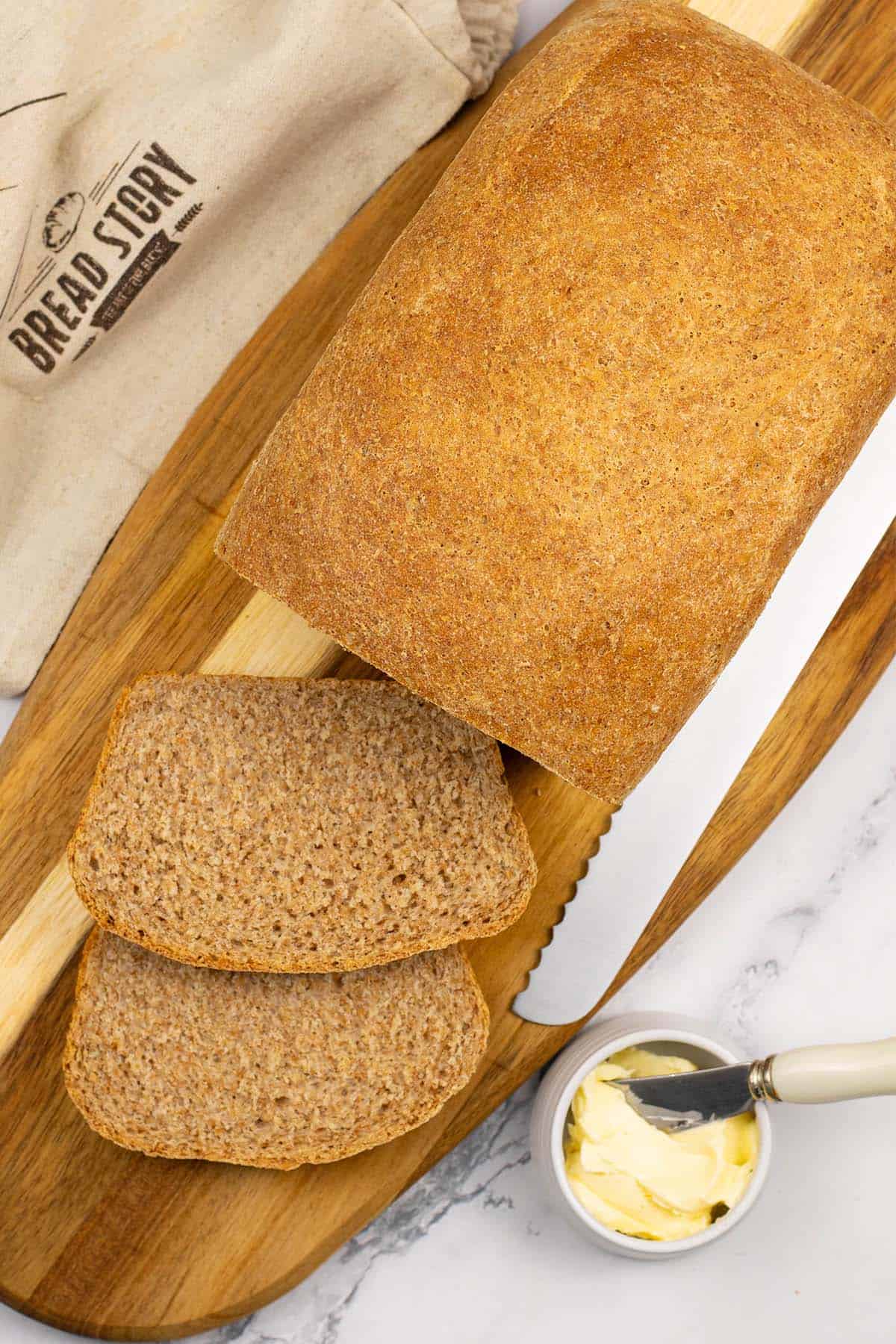 Classic wholemeal bread made in the Thermomix on a board with 2 slices cut and a small dish of butter with butter knife on the side.
