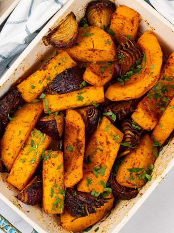 Roast paprika squash and red onions in a rectangle Staub ovenproof dish with a teal and white check towel.