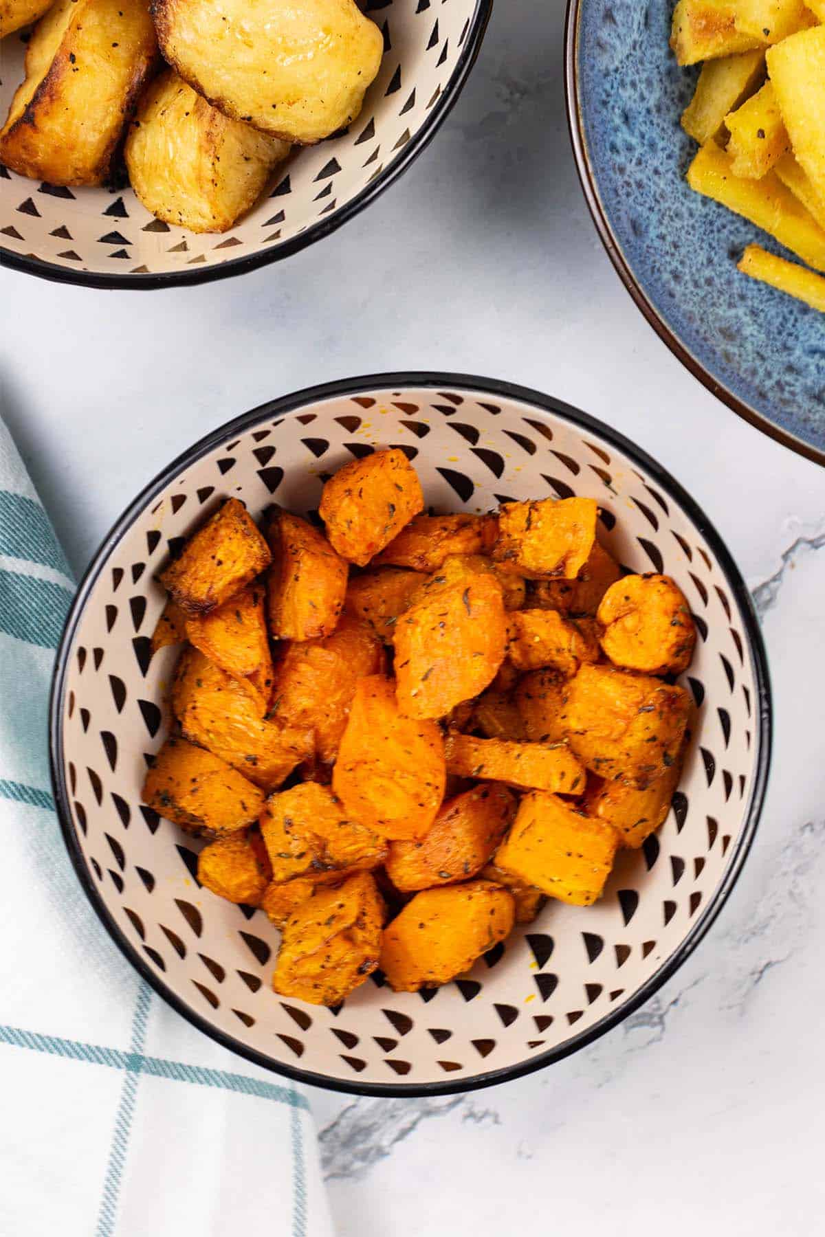 Air fryer carrots and butternut squash in a black and cream patterned bowl with bowls of parsnips and roast potatoes in the background.