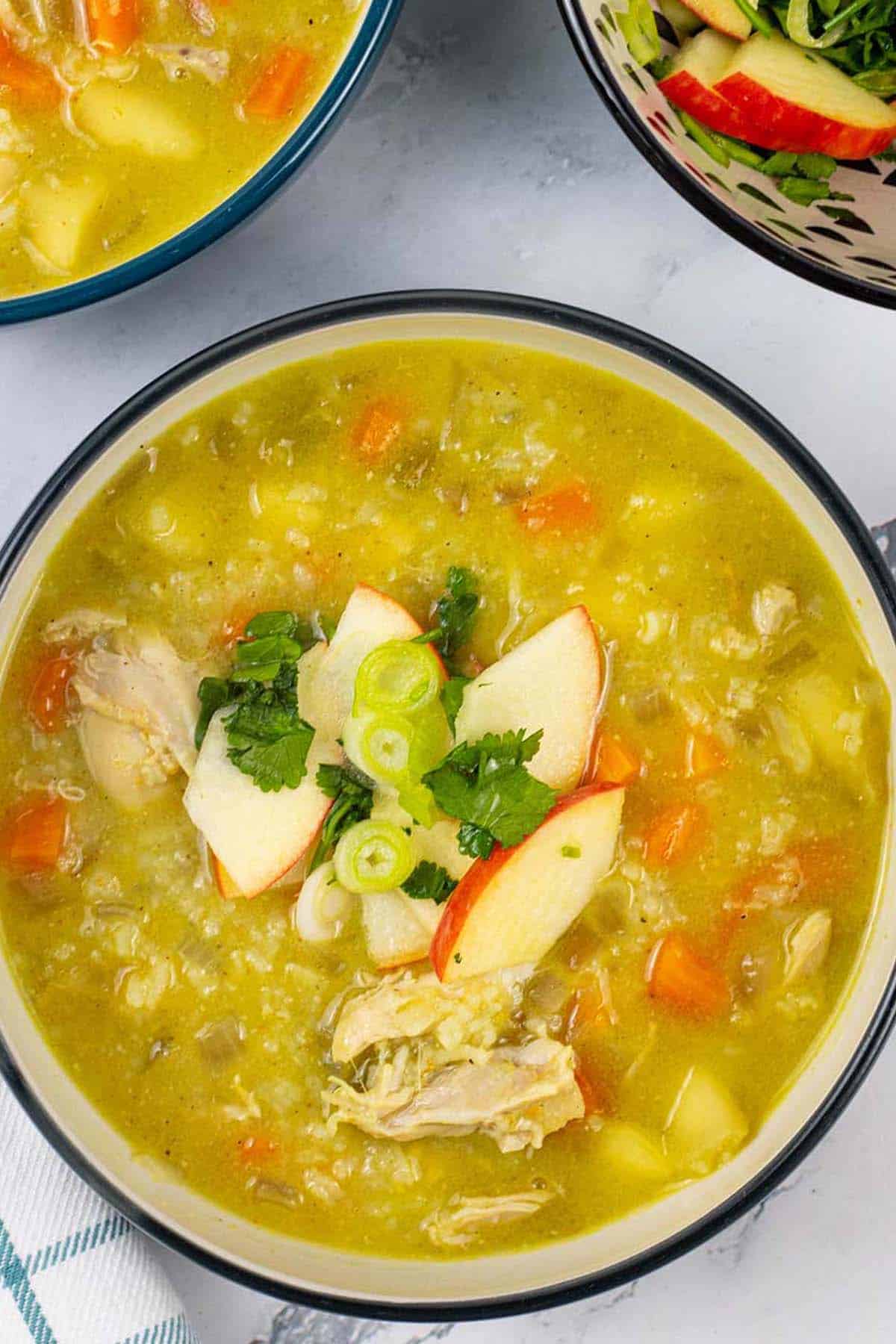 Two bowls of chicken mulligatawny and a bowl of apple relish on the side.