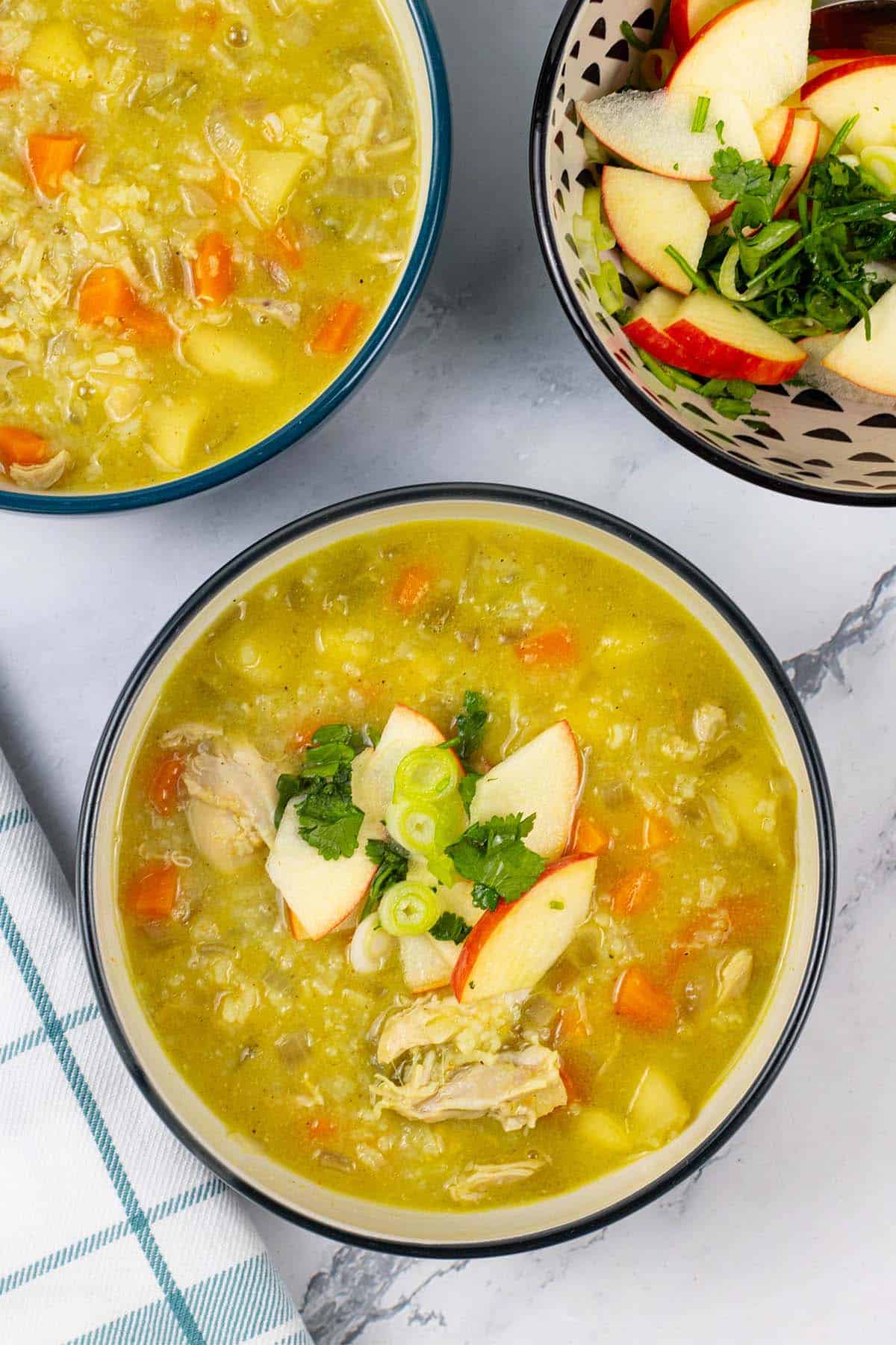 Two bowls of chicken mulligatawny and a bowl of apple relish on the side.