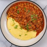 Sausage and white bean ragu with cheesy polenta in a black and cream bowl.