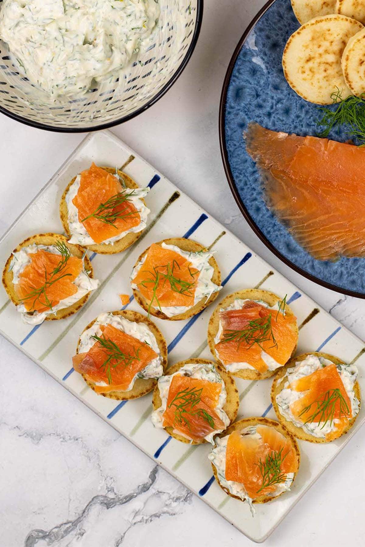 8 smoked salmon and lemon caper cream cheese blinis on a rectangle striped platter.