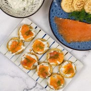 8 smoked salmon and lemon caper cream cheese blinis on a rectangle striped platter.