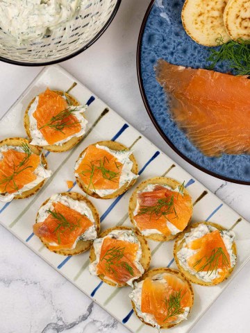 8 smoked salmon and lemon caper cream cheese blinis on a rectangle striped platter.