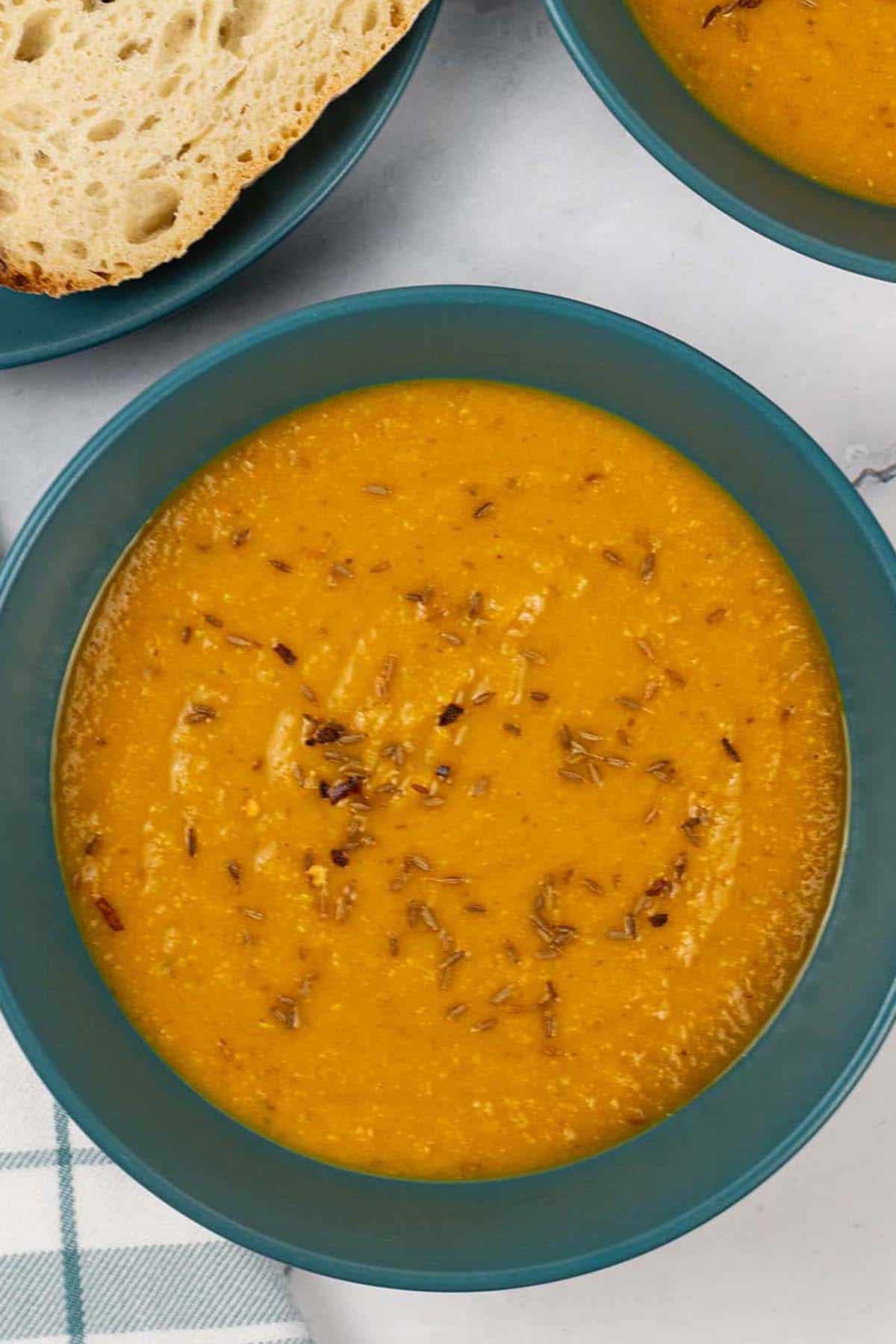 Two bowls of spiced carrot and lentil soup with a plate of sliced crusty bread on the side.