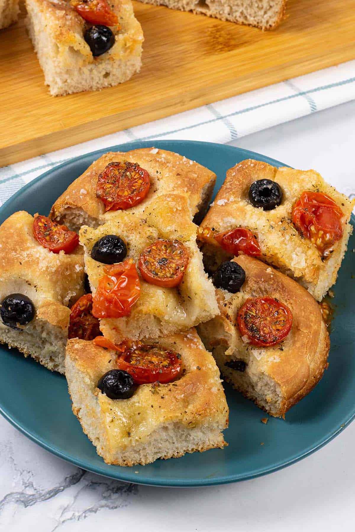 Six slices of tomato and olive focaccia on a teal side plate.