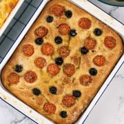 Tomato and olive focaccia in a blue rimmed white enamel roasting tin.