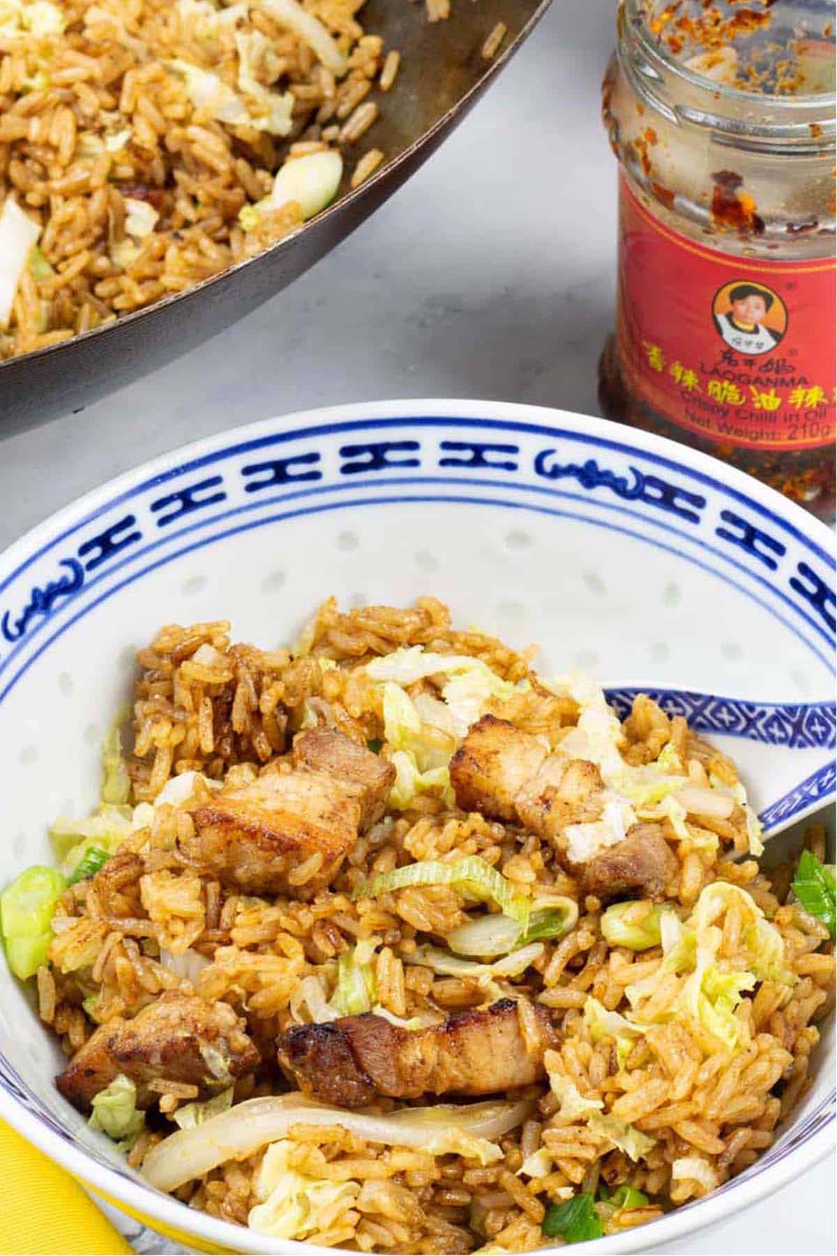 A portion of Cantonese pork belly fried rice in a blue and white oriental bowl with the wok in the background.