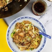 A portion of Cantonese pork belly fried rice in a blue and white oriental bowl with the wok in the background.