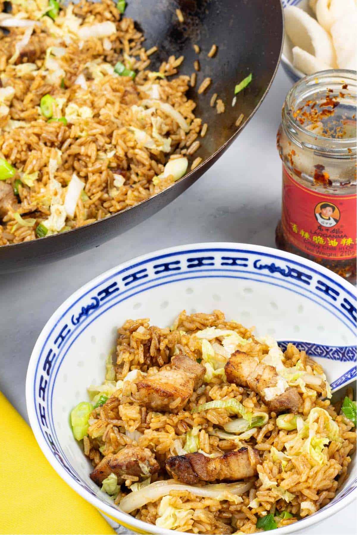 A portion of Cantonese pork belly fried rice in a blue and white oriental bowl with the wok in the background.