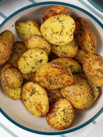 Air fryer thyme roast baby potatoes in a teal and cream serving bowl.