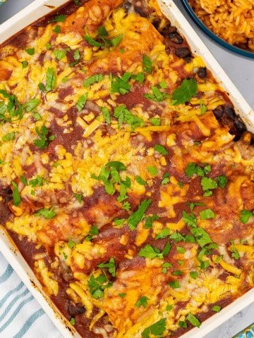 Beef and bean enchiladas in a rectangle Staub ovenproof dish with a bowl of Mexican red rice on the side.