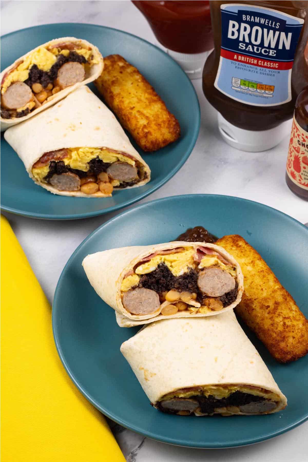 Two portions of breakfast burritos on teal side plates with a cheesy hash brown and blob of brown sauce on the side.