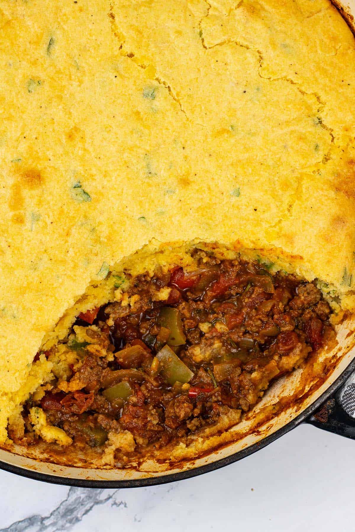 Chilli cornbread pie in a large shallow casserole dish with a wedge of cornbread removed.