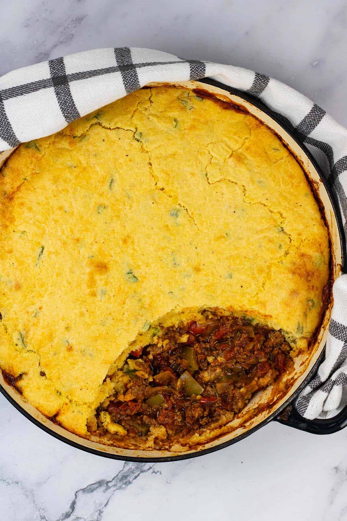 Chilli cornbread pie in a large shallow casserole dish with a wedge of cornbread removed.