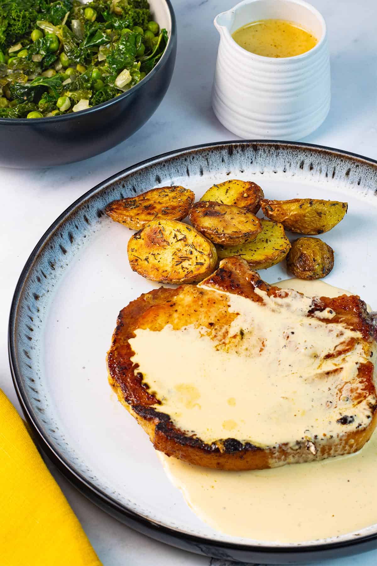 Creamy peppercorn sauce poured over a pan fried pork chop on a white and black patterned dinner plate.