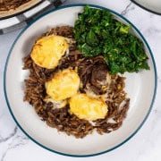 A bowl of french onion meatballs with orzo, with sautéed kale with chilli and lemon on the side.