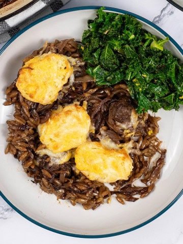 A bowl of french onion meatballs with orzo, with sautéed kale with chilli and lemon on the side.